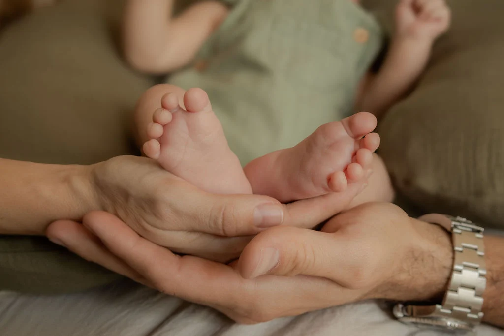 Pequeños pies de un bebé entre las manos de sus papás