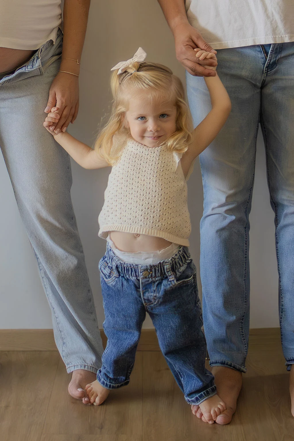 Pequeña de pie tomada de las manos de sus papás