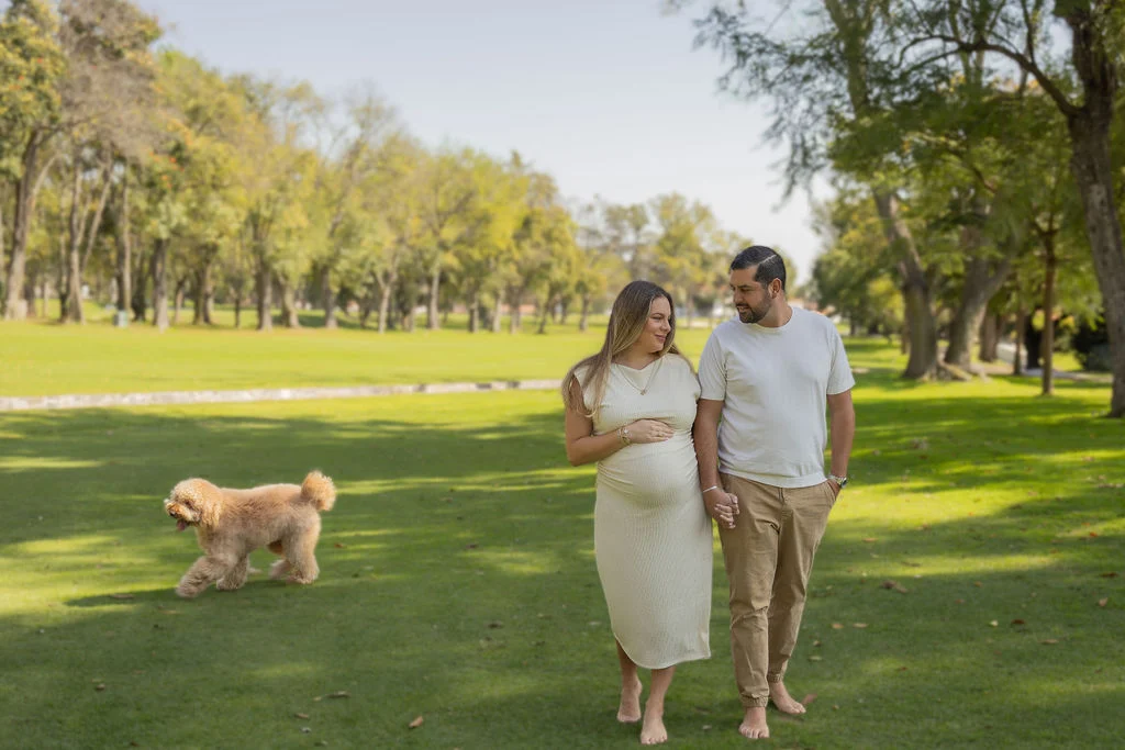 Futuros papás paseando en un jardín con su perro